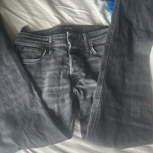 Svarta jeans från Jack & Jones, 29/32 - Snygga svarta jeans från Jack & Jones med klassisk femficksdesign och diskreta slitningar. Jeansen har normal passform och är tillverkade i ett mjukt och slitstarkt bomullsmaterial. Perfekta för dig som gillar en stilren look.