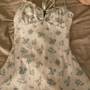 Blommig kortklänning från Gina Tricot - Supersöt kortklänning från Gina Tricot med ljusblå och gröna blommor på vit bakgrund. Pris kan alltid diskuteras vid snabb affär!💕