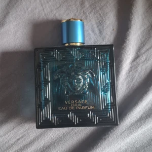 Versace Eros Eau de Parfum 65 ml - Versace Eros Eau de Parfum i en lyxig, blågrön glasflaska med guldiga detaljer och ikoniska Medusa-huvudet i relief. Flaskan rymmer 100 ml och har en stilren, fyrkantig form med geometriskt mönster. Kommer med originalkartong i blått och guld. Priset är inte satt så kom gärna med bud!