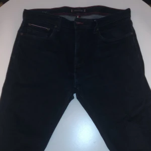 Tommy Hilfiger Bleecker Slim Fit jeans - Snygga mörkblå jeans från Tommy Hilfiger, modell Bleecker Stretch Slim Fit. Jeansen har klassisk femficksdesign, röda kontrastsömmar och diskret logga på bakfickan. Stretchigt material för extra komfort och slim passform som sitter snyggt.