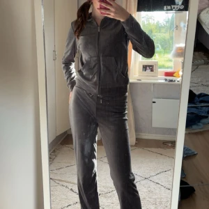 Mörkgrå mjukisset från Gina Tricot - Mysiga mörkgrå mjukisse från Gina Tricot i mjuk velour. Byxorna har normal passform men även tröjan, raka ben och dragsko i midjan för extra komfort. Perfekta för chill dagar hemma eller när du vill vara bekväm men ändå se snygg ut.