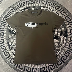  Palm Angels t-shirt - Snygg olivgrön t-shirt från Palm Angels med tryckt logga och coolt drip-effekt på bröstet. Klassisk rund hals och korta ärmar, perfekt för dig som gillar streetwear och vill sticka ut med ett trendigt märke.