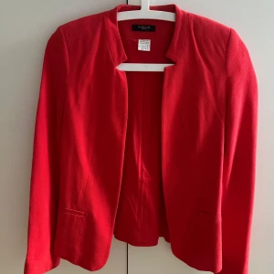 Röd kavaj från La Redoute - Snygg röd kavaj med stilren, öppen front och diskreta fickor. Jackan har lång ärm och är tillverkad i ett strukturerat tyg som ger en modern känsla. Perfekt för att lyfta vilken outfit som helst med en pop av färg. Kavajen är i storlek US 4