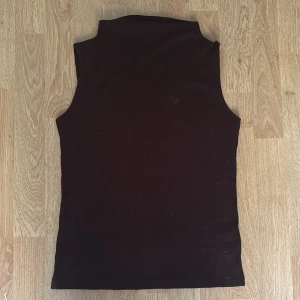 Svart ribbad polotopp från Lindex - Säljer en svart ärmlös polotopp från Lindex i storlek S. Toppen är ribbad och har en hög krage som ger en clean och stilren look. Perfekt att styla med jeans eller kjol för en trendig vibe.