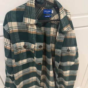 Rutig overshirt från Jack & Jones - Snygg rutig overshirt från Jack & Jones i grönt, beige och brunt. Skjortan har klassisk krage, knäppning framtill och två bröstfickor med knappar. Perfekt att slänga över en t-shirt för en avslappnad look.