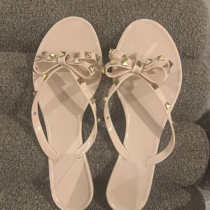 Beiga flippflopps - Snygga beiga flippflopps med en liten liten klack och rosetter framtill med guldiga nitar💕🥰