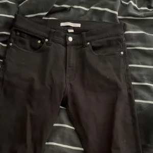 Svarta jeans från Calvin Klein - Svarta jeans från Calvin Klein med klassisk femficksdesign och diskret logga på bakfickan. Jeansen har en slim passform och är tillverkade i ett mjukt bomullsmaterial med lite stretch för extra komfort. Perfekta för en clean och stilren look. Nästan helt nya 