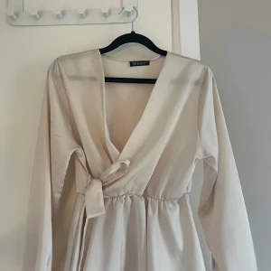 Champagnefärgad omlottblus Missay - Säljer en champagnefärgad omlottblus från Missay i glansigt satinliknande material. Blusen har långa ärmar med resår vid ärmslut, markerad midja och knytband i sidan. Säljer då jag inte tycker den sitter bra på mig och kommer derför inte till användning, endast använd en gång💕
