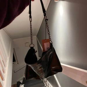 Svart axelväska med kedjedetalj - Snygg svart axelväska i glansigt skinnimitation med croco-mönster. O andvänd.