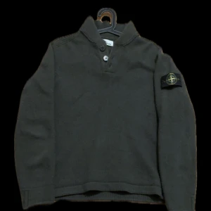 Mörkgrön stickad Stone Island tröja - Säljer en mörkgrön stickad tröja från Stone Island med klassisk patch på vänster ärm. Tröjan har hög krage med tre knappar och långärmad passform. Perfekt för dig som gillar streetwear och vill ha något som sticker ut med snygga detaljer.