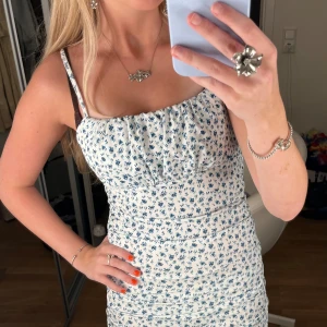 Vit blommig kortklänning  - Supersöt vit kortklänning med blått blommigt mönster och smala axelband. Helt ny💞💞Passar xs och s