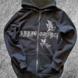 Svart Zip hoodie - Svart zip hoodie i storlek S med strassdetaljer och tryck på framsidan. Tröjan har dragkedja, huva och fickor framtill. Storlek S men stor för storleken. 