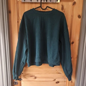 Mörkgrön oversized sweatshirt - Säljer en mörkgrön oversized sweatshirt med rund hals och långa ärmar. Tröjan har en loose passform och är tillverkad i mjuk bomullsmix, perfekt för chill dagar. Enkel och stilren design utan tryck eller mönster.
