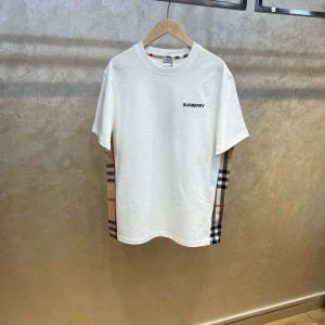 Vit Burberry t-shirt med rutiga sidor - Snygg vit t-shirt från Burberry med klassiskt rutigt mönster längs sidorna och diskret Burberry-logga på bröstet. T-shirten har rund hals och korta ärmar, perfekt för en clean och stilren look.