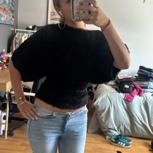 Svart fluffig tröja med vida ärmar - Supermjuk svart tröja med fluffig pälsliknande känsla och vida, nästan halvlånga ärmar. Tröjan är croppad och har en snygg, figurnära passform i midjan. 