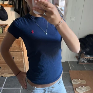 Marinblå t-shirt från Polo Ralph Lauren - Snygg marinblå t-shirt från Polo Ralph Lauren i storlek XS. Tight design med korta ärmar och rund hals. T-shirten har det ikoniska röda Polo-broderiet på bröstet och är gjord i mjuk bomull som sitter tight och bekvämt. Perfekt till jeans eller shorts. Köpt av mig i Ralph Lauren butik så äkta.
