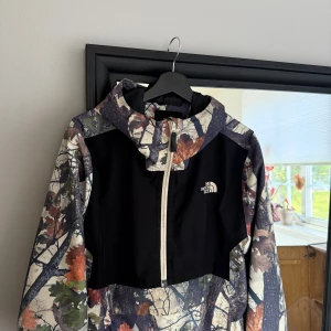  The North Face jacket  - The North Face Waterproof Fanorak Jacket  This technical jacket from The North Face is made from a shell of 100% recycled polyester in a waterproof weave with a comfortable and sporty mesh lining. The jacket has an elasticated hem and cuffs and it has a zippered neckline leading to the drawcord hood. The jacket has a zippered kangaroo pocket and a pouch and it has a graphic logo print to the chest.   This is a slightly relaxed fit