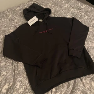 Svart hoodie från YOURTURN med tryck - Svart hoodie från YOURTURN i storlek S med huva och snörning. Framsidan har ett rosa tryck med texten 'ONE COMMUNITY - DIVERSITY MATTERS' och baksidan har ett stort graffiti-inspirerat rosa tryck. Tröjan är tillverkad i mjuk bomull och har långa ärmar. ALDRIG ANDVÄND!!