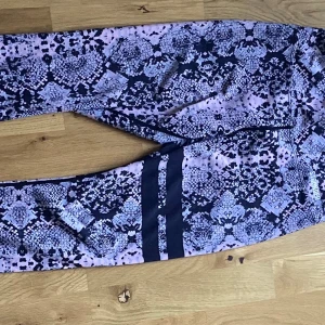 Stronger set  med mönster, storlek  M - Säljer ett snyggt set  från Stronger i storlek medium. De har ett svart och lila mönster, två svarta ränder på ena benet och bred midja. Materialet är stretchigt med 85% polyester och 15% elastan – perfekta för träning eller chill.
