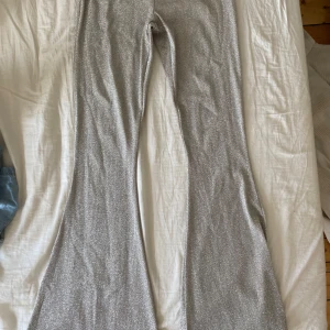 Glittriga silver bootcut byxor - Säljer ett par riktigt snygga bootcut byxor i glittrigt silver. De har en bred utsvängd passform och är perfekta för att sticka ut. Materialet är mjukt och stretchigt syntet som ger en skön känsla. Perfekt för dig som vill ha något extra till din outfit.
