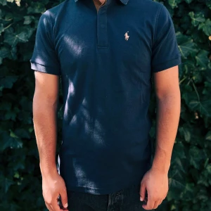 Mörkblå Polo Ralph Lauren t-shirt - Snygg mörkblå t-shirt från Polo Ralph Lauren med klassisk polokrage och korta ärmar. Broderad logga i beige på bröstet. Tillverkad i mjuk bomull som känns skön mot huden. Perfekt för dig som gillar stilren och enkel design.                                                                                                                                                                                Nypris: 1799kr GORILLAPRIZE:920kr            Skick:10/10 oöppnad         KVITTO MEDKOMMER     
