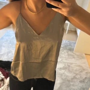 Beige linnetopp i satin-look - Säljer en stilren beige linnetopp med smala axelband och v-ringning både fram och bak. Toppen har en lätt glansig satin-look som ger en lyxig känsla och är perfekt att styla med jeans eller kjol. Enkel och snygg design som passar till många outfits. Aldrig använd och prislapp kvar. 