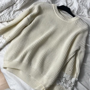 Vit stickad tröja med spetsdetaljer - Superfin vit stickad tröja med breda ärmar och snygga spetsdetaljer längst ner på ärmarna. Tröjan har en rund halsringning och grovstickad struktur som ger en mysig och trendig look. Perfekt för lager-på-lager-stil under kyliga dagar.