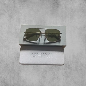 CHIMI solglasögon - Snygga solglasögon från CHIMI med rektangulära gröna linser och tunn guldfärgad metallbåge. Kommer med originalfodral, box och putsduk. Perfekt accessoar för att lyfta din stil och skydda ögonen mot solen.