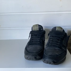 Svarta Valentino Garavani sneakers - Snygga svarta sneakers från Valentino Garavani med coola detaljer i både skinn och mocka. Skorna har svarta snören, rund tå och en robust sula med mönster. Perfekta för dig som gillar exklusiva och stilrena sneakers med edge.