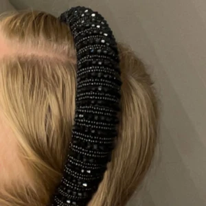 Svart glittrigt diadem med pärlor - Snyggt svart diadem med glittriga svarta pärlor och stenar som ger en lyxig känsla. Diademet är brett och vadderat för extra volym och statement-look. Perfekt accessoar för att lyfta din outfit med lite extra bling.