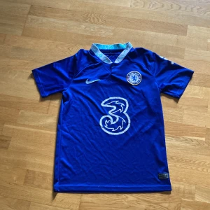 Chelsea tröja Nike xs/s - Chelsea FC matchtröja i starkt blå färg med vit logga från Nike och klubbmärke på bröstet. Stort vitt sponsortryck på framsidan och mönstrad krage med ljusblå detaljer. Kortärmad och tillverkad i lätt, ventilerande polyester.