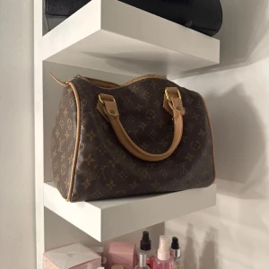 Brun Monogram väska - Säljer en klassisk handväska i brunt monogrammönster med ljusbruna skinnhandtag och detaljer. Väskan har guldfärgade metalldetaljer och dragkedja upptill. Perfekt storlek för att få plats med allt du behöver.
