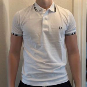 Vit Fred Perry piké med svarta detaljer - Vanlig vit fred perry piké. Tröjan är helt ny. säljer även ut andra saker från min gaderob så kolla gärna min sida och se om du hittar något du gillar!