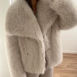 Beige fuskpälsjacka - Zara - Lyxig trendig beige fuskpälsjacka från Zara i storlek L (funkar på mig som annars brukar ha S på jackor). Jackan har en mjuk och fluffig känsla med bred krage och rak passform. Perfekt för att hålla sig varm samtidigt som den ger en elegant och trendig look.  En riktig statement-jacka som passar både till vardags och festligare tillfällen.