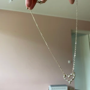 Halsband med hjärthänge i guld med pärlor - Sött halsband med tunn guldfärgad kedja och ett hjärthänge dekorerat med små pärlor. Perfekt accessoar för att ge en romantisk touch till din outfit.