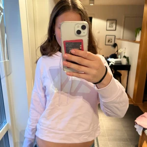 Ljusrosa croppad hoodie från Adidas - Säljer en ljusrosa croppad hoodie från Adidas med vit logga på bröstet. Tröjan har långa ärmar, huva med dragsko och ribbade muddar. Perfekt för en avslappnad och sportig stil.