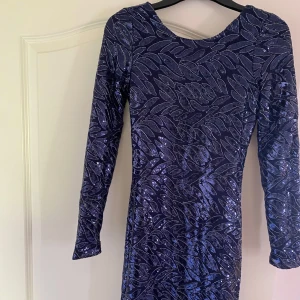 Blå glittrig långärmad klänning från Make Way - Säljer en blå glittrig klänning från Make Way med lång ärm och djup rygg. Klänningen har ett vackert mönster av paljetter i bladform och är figurnära. Perfekt för dig som vill sticka ut med stil. Ordinarie pris för klänningen är 399kr men säljer den för mycket billigare. Klänningen har även prislappen kvar.