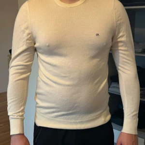 Beige stickad tröja från Calvin Klein - Säljer en stilren beige stickad tröja från Calvin Klein. Tröjan har rund halsringning, diskret CK-logga på bröstet och långa ärmar. Storlek L