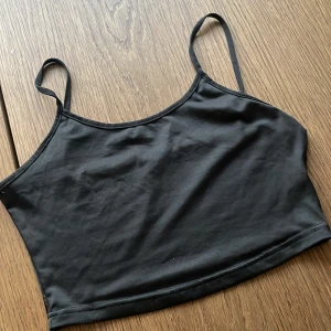 Svart croppad linnetopp - Säljer en svart croppad linnetopp med tunna axelband. Enkel och stilren design som passar perfekt till sommaren. Mjuk och stretchig känsla i materialet.