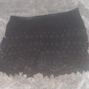 Svarta spets-shorts från Gina Tricot - Säljer ett par svarta shorts från Gina Tricot med vacker spets och blommigt mönster. Shortsen har en feminin look med fina detaljer längs kanten och är perfekta för varma dagar.