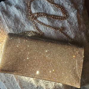 Guld glittrig handväska - Från Zalando, använd 1 gång. Nypris 499 kr. Säljer för 249kr. Man kan ta av guldbandet o ha den som en kuvertväska💛