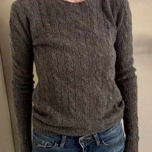 Grå kabelstickad tröja från Polo Ralph Lauren - Säljer en klassisk grå kabelstickad tröja från Polo Ralph Lauren. Tröjan har rund halsringning, lång ärm och diskret broderad logga på bröstet. Perfekt för lager-på-lager och enkel att matcha med jeans eller kjol.