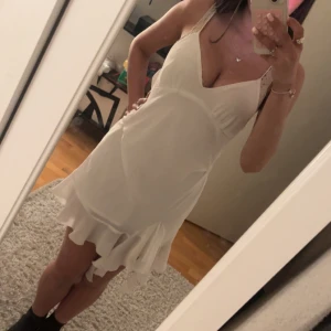 Vit kortklänning med volang från Zara - Säljer en söt vit kortklänning från Zara med smala axelband och v-ringning. Klänningen har en volangdetalj nertill och är perfekt för varma dagar. Säljer för att den inte kommer till användning! 💓💓