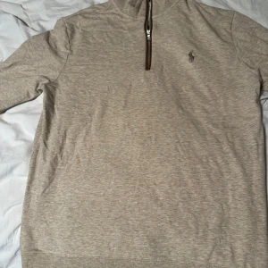 Beige halvzip tröja från Polo Golf Ralph Lauren - Snygg beige långärmad tröja från Polo Golf Ralph Lauren med halv dragkedja och broderad logga på bröstet. Slim fit-modell som passar perfekt till en stilren look. Mjuk och bekväm, perfekt för lager-på-lager. Man kan ha den som träningströja men även till skolan. Storleken är M som sitter slim fit 