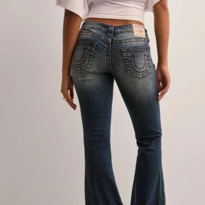 Blå bootcut jeans från True Religion - Säljer ett par klassiska blå bootcut jeans från True Religion med röda sömmar. Dem är ultra low waist. Original pris 1400kr. Dem är i storlek W25 och är andvänd 2 gånger bara! Kontakta mig för fler bilder på hur dem ser ut i verkligheten💕