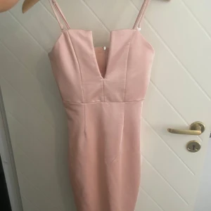 Ljusrosa tight klänning med v-ringning - Säljer en ljusrosa klänning med smala axelband och djup v-ringning. Klänningen är figurnära och har dragkedja i ryggen. Perfekt för dig som vill ha en stilren och elegant look. Den skimrar, banden är avtagbara. Passar s också. Endast använd 1 gång 