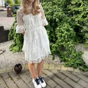 Vit spetsklänning med volang perfekt till studenten elelr Konfirmation  - Superfin vit kortklänning i spets med volanger och hög krage. Klänningen har trekvartsärm med volangdetaljer och är tillverkad i ett lätt, transparent spetsmaterial. Perfekt för sommarens alla tillfällen.klänningen är från bubbelroom och är i väldigt bra skick. Pris kan diskuteras 💗💗endast använd en gång.ordinarie pris är 699