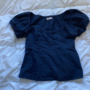 Mörkblå blus från Nelly - Säljer en mörkblå blus från Nelly med puffiga korta ärmar och knappar framtill. Blusen har en feminin passform med markerad midja.