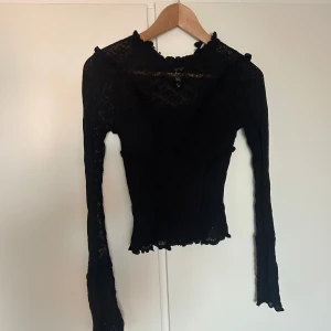 Svart spetsig långärmad topp med volangdetaljer - Säljer en svart långärmad topp med spets och volangdetaljer. Toppen har transparenta ärmar i spets och en figurnära passform. Perfekt för dig som gillar detaljer och en lite mer dressad look.