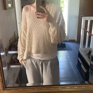 Beige stickad croppad tröja - Säljer en beige stickad tröja med v-ringning och löst, croppat passform. Tröjan har ett genomgående hålmönster och långa ärmar. Perfekt för lager-på-lager och en avslappnad stil.